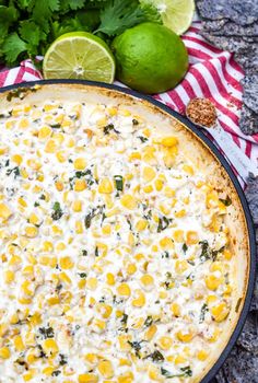 a corn and cheese casserole in a cast iron pan with limes on the side