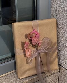 a present wrapped in brown paper with pink flowers tied to the front and side of it