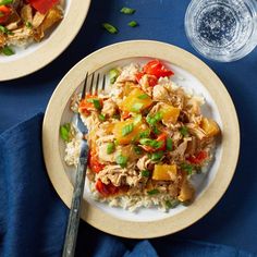 two plates filled with rice, chicken and veggies next to a glass of water