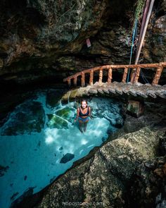 a person in a body of water with a wooden bridge above them that is surrounded by rocks