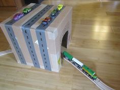 a cardboard box that has cars on it and a train coming out of the tunnel