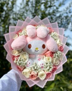 a person holding a pink and white teddy bear in a wreath with roses on it