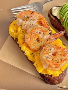 there is a sandwich with shrimp on it next to a fork and avocado