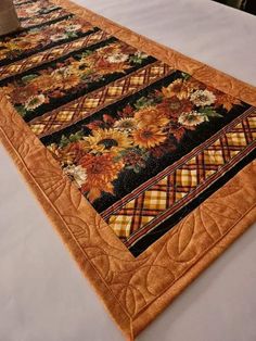 a quilted table runner with sunflowers and plaid on the border is sitting on top of a bed