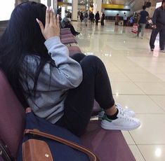 a woman sitting on top of a purple chair next to an airport terminal holding her cell phone