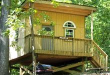 a tree house in the woods with a car parked on the porch and stairs leading up to it