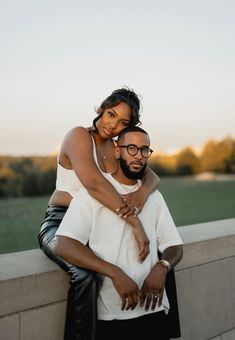 a man holding a woman on his back while she is leaning against a stone wall