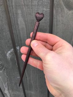 a person holding a stick with a heart on it's end in front of a wooden fence