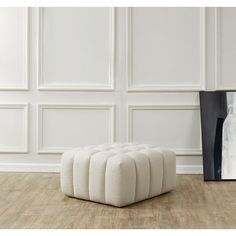 a white ottoman sitting on top of a hard wood floor next to a framed photograph