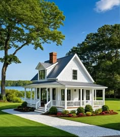 a white house sitting on top of a lush green field next to a body of water