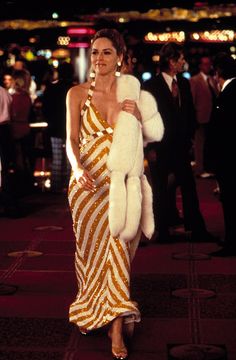 a woman in a gold and white dress is walking down the street with a fur stole around her neck