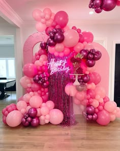 a pink and purple balloon arch with happy birthday written on the front, surrounded by balloons