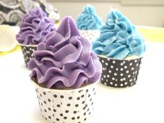 three cupcakes with purple and blue frosting on them sitting on a table