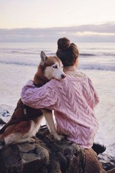 a woman sitting on top of a rock next to a brown and white husky dog