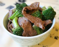 a white bowl filled with beef and broccoli on top of a yellow place mat