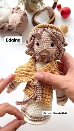 a crocheted doll is being held up by someone's hand with other items in the background