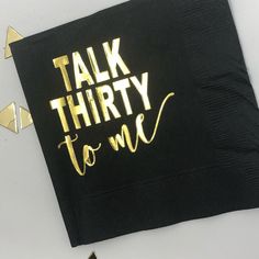 a black napkin that says talk thirty to me with gold foil lettering on the front