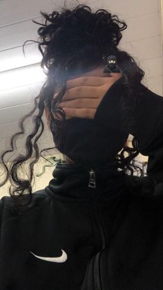 a woman with curly hair wearing a black hoodie and holding her face up to the camera