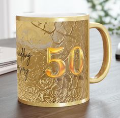 a golden 50th birthday mug sitting on top of a table next to a laptop computer