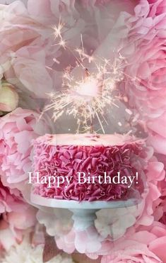 a pink birthday cake with sparklers on top and flowers in the background, says happy birthday