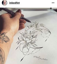 a person with a pencil in their hand writing on paper that has a flower tattoo