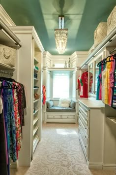 a walk in closet with lots of drawers and clothes hanging on the shelves, along with a chandelier