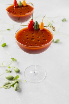 two glasses filled with red sauce and garnishes