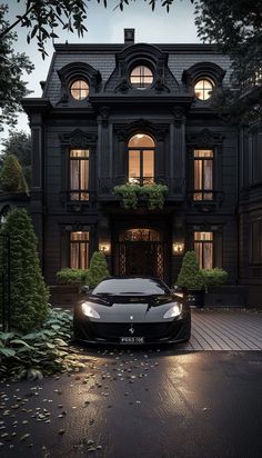 a black sports car is parked in front of a large house at night with its lights on