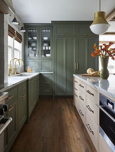 a kitchen with green cabinets and white counter tops, wood flooring and gold accents