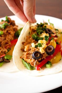 a tortilla filled with meat, vegetables and olives is being held by someone