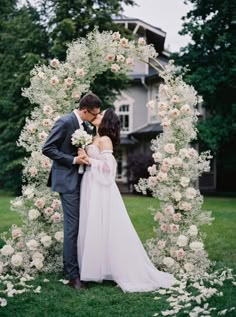 a bride and groom kissing in front of a floral arch with white flowers on it