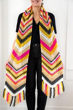 a woman standing in front of a white wall wearing a multicolored shawl