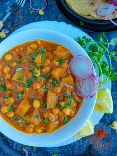 a white bowl filled with stew next to a tortilla and cilantro