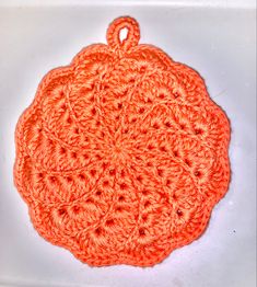 an orange crocheted doily on a white surface with a hook in the middle