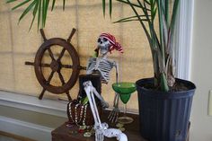 a skeleton is sitting on a table next to a potted plant and a steering wheel