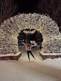 a woman standing in front of a white arch covered in snow at night with her arms outstretched