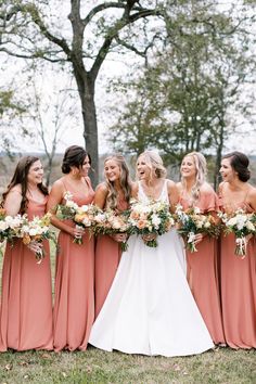 a bride and her bridesmaids laughing together in front of the trees at their wedding