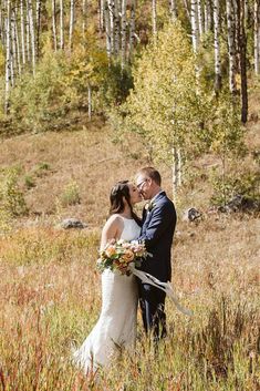 a bride and groom are standing in the tall grass with their arms around each other