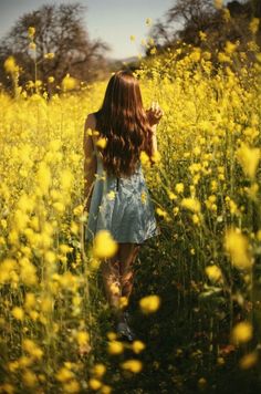 a woman walking through a field of yellow flowers with her hair blowing in the wind