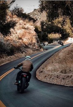 a man riding a motorcycle down a curvy road next to a hill and trees