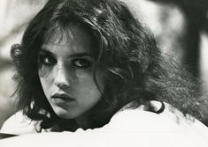 black and white photograph of a woman with long hair looking at the camera while holding her hand on her shoulder