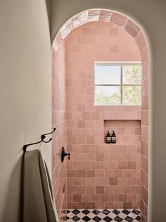 a pink tiled shower with black and white checkerboard flooring is seen through an arched window