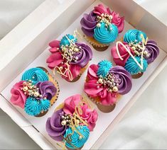 six cupcakes in a box decorated with pink, blue and purple icing