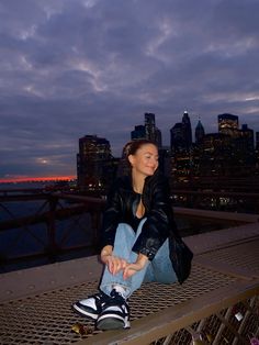 a woman sitting on top of a metal bench next to a cityscape at night