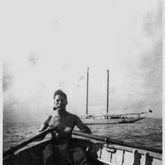 a man sitting in the front of a boat on top of the ocean next to a sailboat