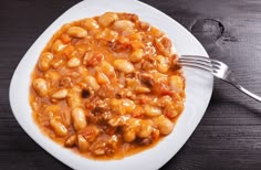 a white plate topped with beans and meat next to a fork on top of a wooden table