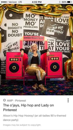 a woman sitting on top of a pink chair in front of a wall with gold balloons