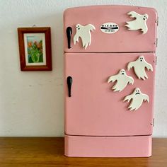 an old pink refrigerator with ghost magnets on the front and bottom doors, sitting on a wooden table