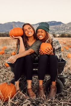 two women sitting in a field with pumpkins