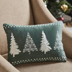 a green pillow with white trees on it sitting on a chair in front of a christmas tree